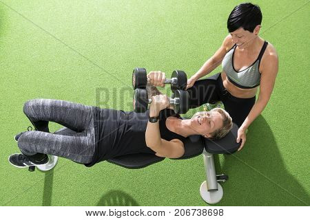 Overhead shot of a woman performing dumbbell chest flyes as her personal trainer watches