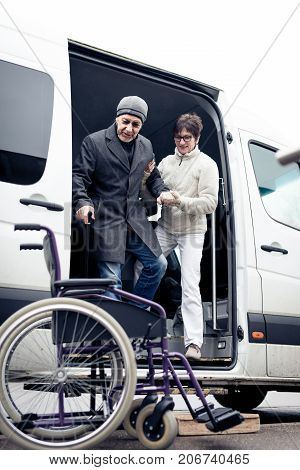 nurse helping senior man exit a van and get to his wheelchair