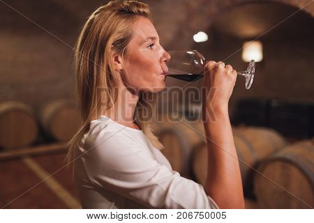 Beautiful woman oenologist tasting wine in winegrower cellar