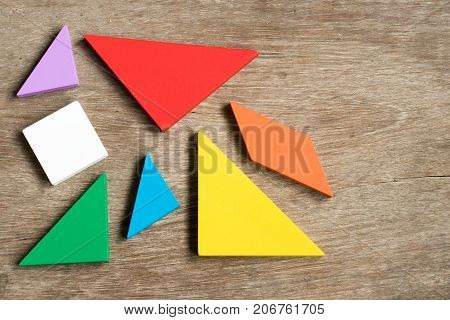 Straggled tangram puzzle wait to complete the shape on wood background
