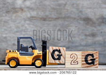 Yellow plastic forklift hold letter G to complete word G2G (Government to government) on wood background