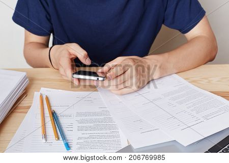 Cropped Image Of Smart Phone In Man`s Hands. Busy Male Enterpreneur Sits At Work Place, Uses Modern