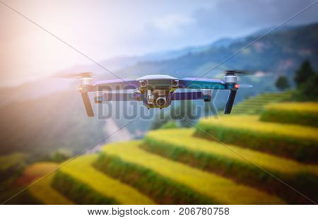 Modern RC Drone / Quadcopter with camera flying on rice fields terraced at sunset in Mu Cang Chai YenBai Vietnam.