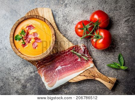 Spanish tomato soup Salmorejo served in olive wooden bowl with ham jamon serrano on stone background. Top view.