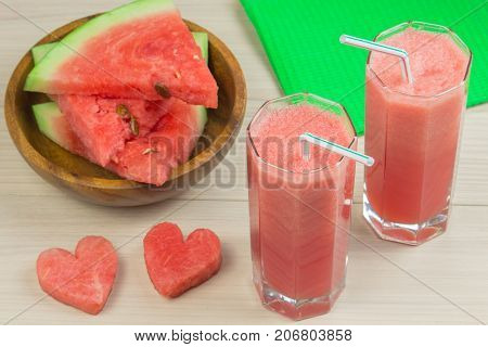 Two hearts, Watermelon juice in two glass glasses with a straw on a light wooden background, a delicious cocktail, a plate with slices of ripe watermelon on the table