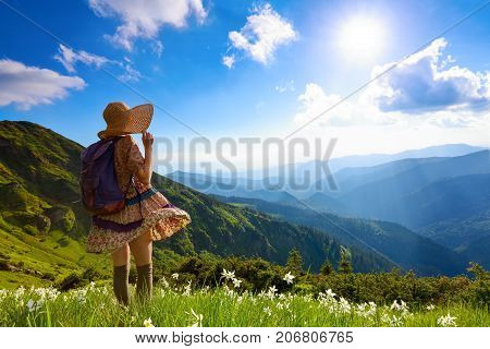 The lawn with white daffodils in the high mountains landscapes. The girl in overknees stockings romantic dress back sack and straw hat.