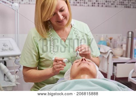Microcurrent face treatment. Cosmetician working and smling. Skin anti aging strategies.