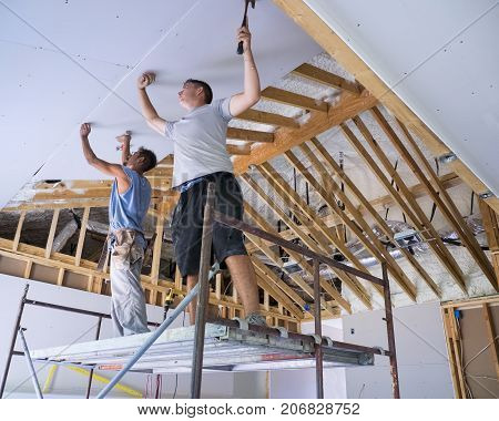 Two construction workers standing on a scaffold putting up sheetrock on a cathedral ceiling.