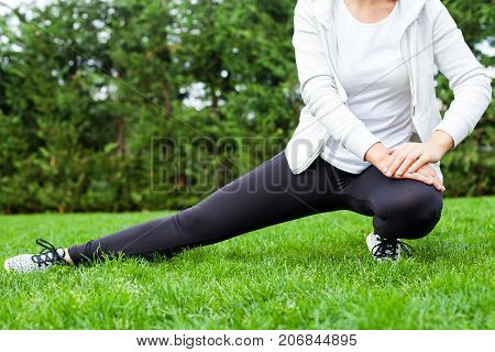 Young female warming up before workout in the park outdoor stretching leg muscles
