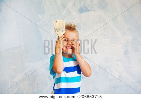 The Child Paints The Blue Wall With A Roller. The Boy Holds A Large Brush For Painting. Home Repairs