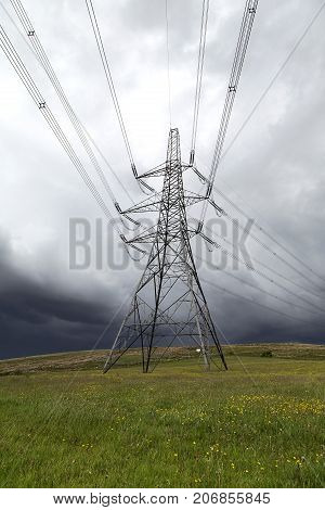 Single electricity pylon in a field with a cloudscape background in a vertical format