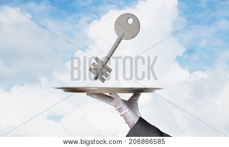 Closeup of waiter's hand in white glove presenting stone key symbol on metal tray with blue cloudy skyscape on background. 3D rendering.