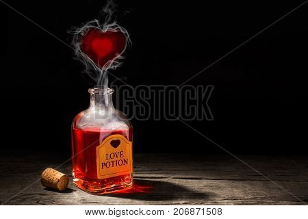 Love potion is red in a bottle. The fragrance of the elixir evaporates and draws from the smoke a heart symbol. Valentine's Day. Copy space for text