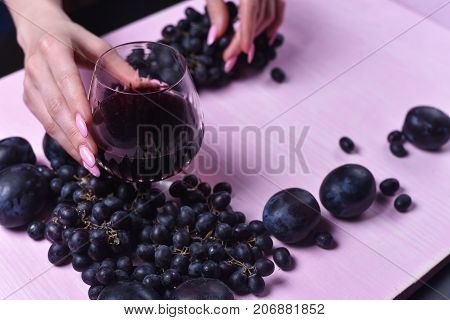 composition of wine, grape and plums on a pink background