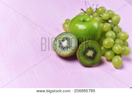 composition of kiwi, grape and apple on a pink background