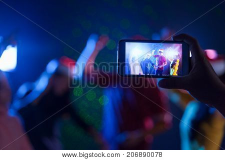 Right hand holding smartphone camera snap shot photo memories people christmas party celebrating bancing together group in midnight club Live social online concept.