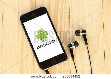 Kiev Ukraine - May 22 2015: iPhone with Android logotype on its screen and headphones on wooden background