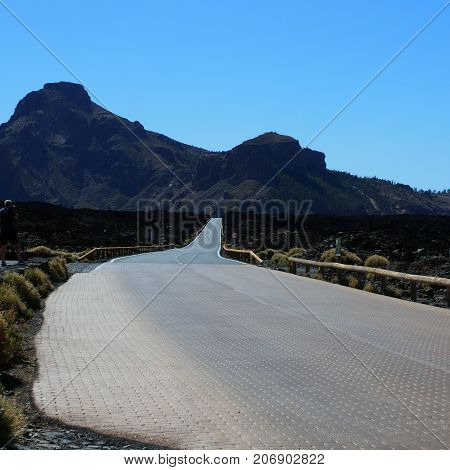 empty winding curced road with distant mountains and blue sky in teide national park in tenerife