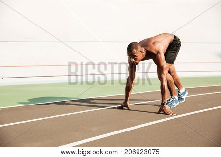 Young musculary african sports man in starting position ready to start on sports track at the stadium