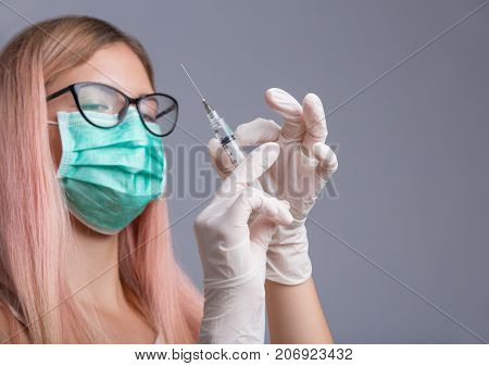 Doctor or nurse in face mask holding syringe isolated over gray