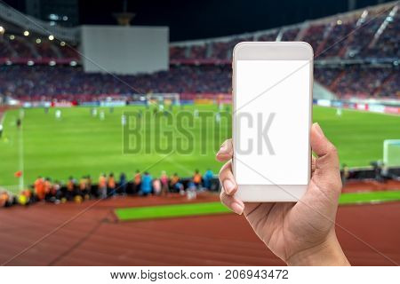 Female hand holding mobile smart phone touch screen on blurred of action photographer taking photo at player in Abstract blurred photo of soccer stadium sport background concept