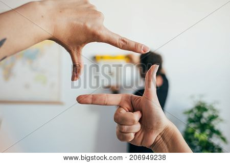 Woman helps her partner or boyfriend or husband to hang painting on wall of their new house or flat starting new life she is framing the photo with her fingers