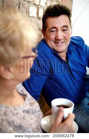 Smiling senior couple sitting in home and drinking coffee or tea.