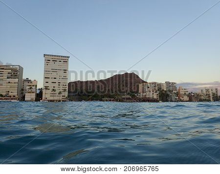 Wavy water on ocean off Kaimana Beach with hotels condos and Diamondhead line the shoreline at dusk on Oahu Hawaii.