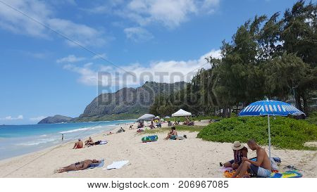 WAIMANALO - May 29 2016: People play in water and sunbath as Gentle wave lap on Waimanalo Beach looking towards Rabbit island and Rock island on a nice day Oahu Hawaii. May 29 2016