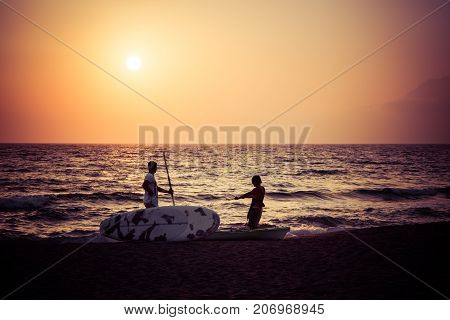 Two silhouttes of men in the sunset with surf boards at a sandy beach, Komos, Crete, Greece