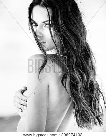 Sexy brunette girl in white swimsuit posing on a beach in black and white