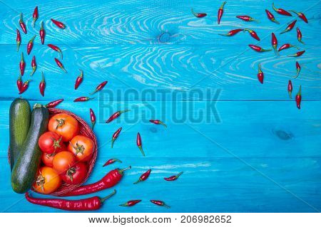 Beautiful composition of harvest autumn vegetables: red tomatoes, chili peppers, green zucchinis on a blue wooden background. Copy space.