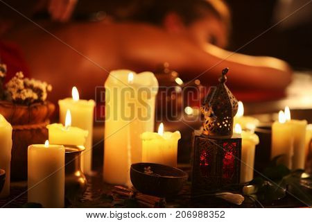 Massage of woman in spa salon. Girl on candles background treats problem back. Luxary interior with working masseuse. Shirodhara Pot background. Candles in foreground. Alternative medicine.