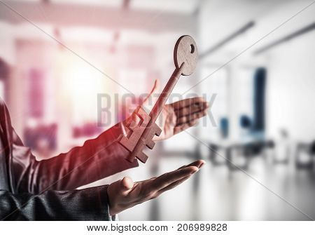 Business woman in black suit keeping big stone key in hands with office view and sunlight on background. Mixed media.