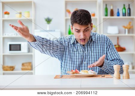 Young husband eating tasteless food at home for lunch