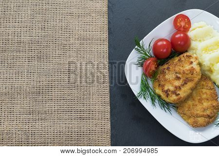 Two juicy fried meat patties on a white plate with cherry tomatoes and mashed potatoes.