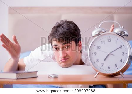 Man in bed frustrated suffering from insomnia with an alarm cloc