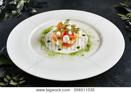 Beautiful Serving Italian Cuisine Dish of Salmon Millefeuille with Cream Cheese Mousse, Arugula and Capers. Exquisite Trout Sashimi of Sliced Red Fish on Natural Dark Stone Background