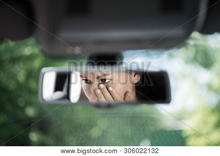 Reflection Of Young Woman With Crying Eyes Covering Her Face With Hands In The Car Rear View Mirror.