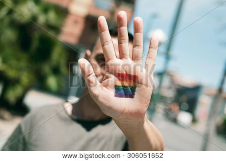 closeup of a young caucasian person with a rainbow flag in the palm of his or her hand, in front of his or her face, on the street at daytime