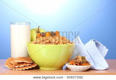 leckere Cornflakes in grüner Schale, Äpfel und Glas Milch auf Holztisch auf blauem Hintergrund