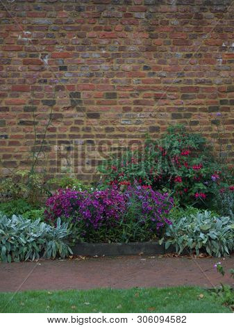 Portrait Image Of Garden Wall With Flowerbed And Path In Foreground