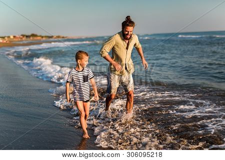 Happy Father And Son, Man & Boy Child, Running And Having Fun In The Sand And Waves Of A Sunny Beach