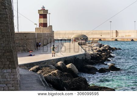 Monopoli, Italy - July 6 2018: Man Fishing In Front Of Lighthouse In Monopoli Port Near Castle Of Ca