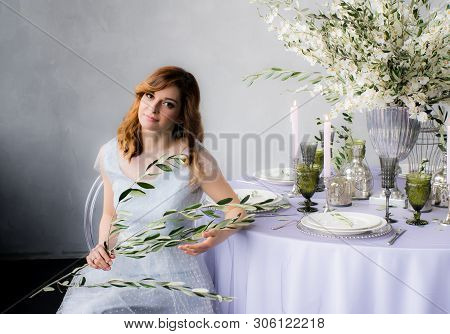 Sitting Bride With Olive Branch In Hands  And Wedding Decorations For Banquet With Sakura, Candles A