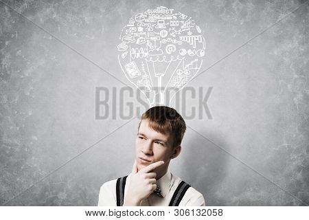 Redhead Student Thinking About Some Problem. Clever Boy On Background Of Grey Wall With Idea Lightbu