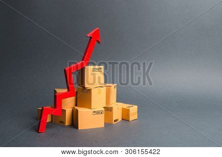 A pile of cardboard boxes and a red up arrow. The growth rate of production of goods and products, increasing economic indicators. Increasing consumer demand, increasing exports, imports. sales rise