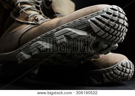 Photo of brown suede military tactical boots with protector texture standing on black surface background close up view.