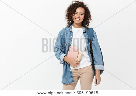 Portrait of a pretty cheerful casual african girl carrying backpack standing isolated over white background, holding textbooks