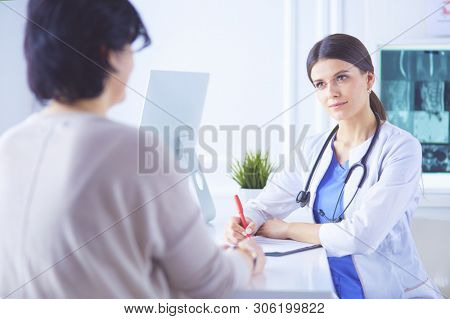Doctor and patient discussing medical problems in a hospital consulting room. Doc filling in a patient's form